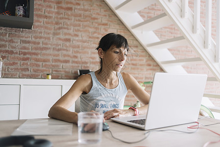 在家使用笔记本电脑的妇女注意力工作咖啡杯桌子低角度手机上网居家机动性电子邮件图片