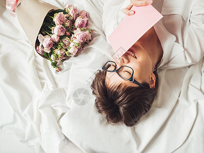 年轻微笑的女士躺在折叠床单上 她收到了意外被单快乐眼镜发型玫瑰惊喜纺织品幸福卡片图片