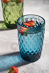 两个绿色和蓝色几何玻璃杯 配有淡水和草莓玻璃反射饮具水果饮料石头阳光杯子静物奢华图片