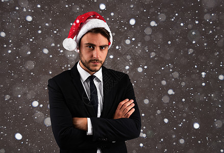 穿着西装和圣诞老人帽子的年轻英俊caucacians男子 在演播室里站在灰色背景上 胸前面贴着严肃的脸部折臂图片