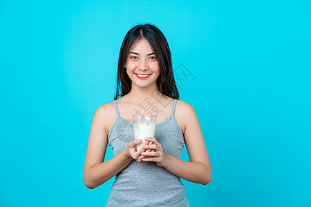 有吸引力的亚洲年轻女子 以孤立的蓝色 喝着牛奶图片