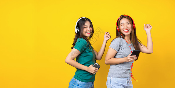 两个快乐的亚洲人 带着无线头号头灯微笑的年轻女人朋友耳机幸福同志乐趣女性情感手机友谊电话图片