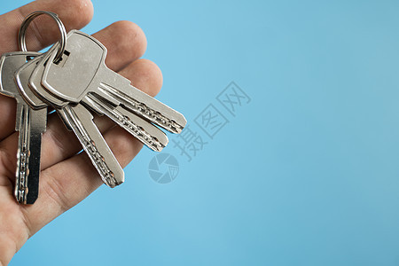 男士手拿着一组蓝色背景的钥匙 房地产经纪人为客户提供公寓钥匙 专注于按键 房地产经纪人手中的一串钥匙家庭建造代理人金融财产住房房图片
