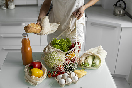 礼盒打开女人从市场回来 在家里的厨房里打开一个装满蔬菜的可重复使用的食品袋 零废物和无塑料概念 女孩拿着带蔬菜的网眼棉购物袋回收杂货店购背景