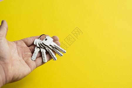 男士手拿着一组黄色背景的钥匙 房地产经纪人为客户提供公寓钥匙 专注于按键 房地产经纪人手中的一串钥匙贷款建造建筑房子男人代理人销图片
