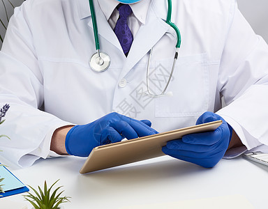 身穿白色医疗大衣的医生坐在一张桌子上 并举着名人表滚动电脑技术屏幕软垫男性办公室医师诊所卫生图片