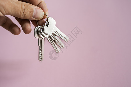 男士手拿着一组粉红色背景的钥匙 房地产经纪人为客户提供公寓钥匙 专注于按键 房地产经纪人手中的一串钥匙贷款住宅男人建造抵押销售房图片