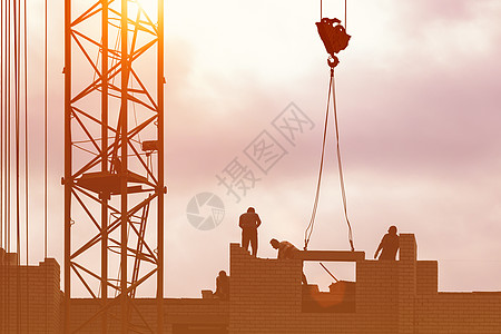 在日落天空背景下建一座建筑 由建筑工人组成的团队的轮廓和一台起重机组成男人团体日落工程施工工作太阳调子男性就业图片