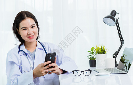 医生用智能手机工作时微笑的女医生电脑女性从业者技术医院诊所药品男人办公室短信图片
