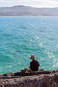 在A Marina从破水岩中捕鱼的年轻男性海洋海岸旅游季节支撑爱好男人钓鱼假期垂钓者图片
