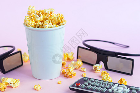 3d电影效果粉色表面有爆米花的纸杯 附近有3D眼镜和电视遥控器 在隔离区看电影咖啡盒子生态笔记本电脑小吃耳机朋友们饮料玉米背景