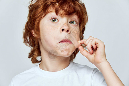 红发男孩拉着脸颊 用手指动脉的刺痛和紧贴的裁剪白色T恤衫图片