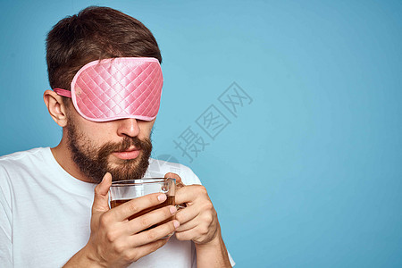 男人脸上戴着粉红睡面具 手手里拿着一杯茶 种植近视蓝底背景成人微笑工作室工作杯子胡须男生商务闲暇男性图片