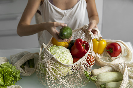 在家里厨房的桌子上 女人拿着鸡蛋托盘 上面放着可重复使用的购物袋和蔬菜 零废物和无塑料概念 蔬菜网眼棉质购物包 生态购物者浪费环图片