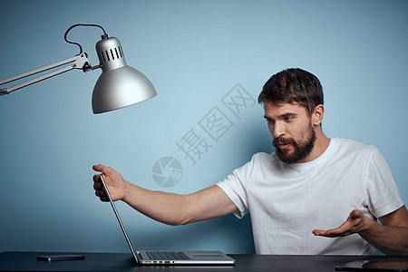 一名男子 在蓝背景和灯灯办公室的桌子上用笔记本电脑商务职场金融商业工作室设计师成人职业房间情感图片