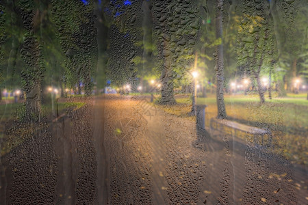 带灯笼和长凳的无重点夜间公园玻璃雨滴阴雨窗户天气背景长椅辉光流动水滴图片