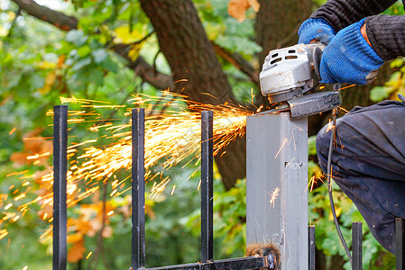 手工业者在绿公园的模糊背景上用圆盘角研磨机切割金属柱金属图片