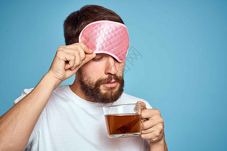 男人脸上戴着粉红睡面具 手手里拿着一杯茶 种植近视蓝底背景胡子饮料潮人幸福成人男性商务微笑工作闲暇图片