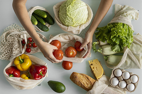 女人的手 拿着一个可重复使用的食品袋 在家里的厨房里放着蔬菜 把西红柿拿出来 零废物和无塑料概念 蔬菜网眼棉质购物包 生态女士女图片
