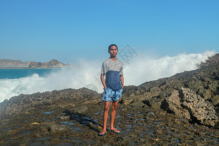 海浪拍打着圆形的岩石 溅起水花 一个年轻人站在多岩石的海岸上 海浪拍打着悬崖支撑海洋碰撞石头运动旅行海滩冲浪管子活力图片