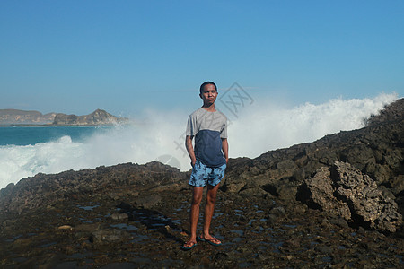海浪拍打着圆形的岩石 溅起水花 一个年轻人站在多岩石的海岸上 海浪拍打着悬崖蓝色飞溅天空海洋风暴运动波浪海景碰撞天气图片
