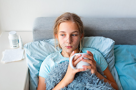 患有高发烧和头痛患病的十几岁少女在床上躺着 喝杯热茶女性毯子疾病枕头童年说谎感染保健药品温度图片
