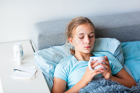 患有高发烧和头痛患病的十几岁少女在床上躺着 喝杯热茶保健女性卫生感染枕头药品温度说谎前额疾病图片