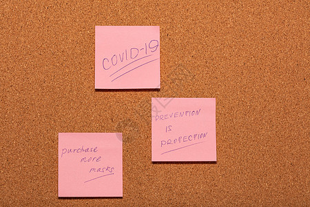 Covid-19 预防就是保护 并提醒购买更多面具 手写在软木告示板上的三张粉色贴纸上图片