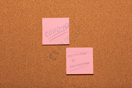 Covid-19和Prevention是保护手写在软木告示板上的两张粉色贴纸上图片