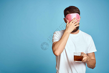 男人脸上戴着粉红睡面具 手手里拿着一杯茶 种植近视蓝底背景男性工作商业商务胡须工作室成人咖啡杯子头发图片