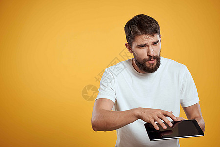 在白色T恤衫上用黄色背景的平板牌男子 商务人士触摸屏幕触摸板的新科技男人工作室互联网展示商务办公室成人衬衫药片商业背景图片