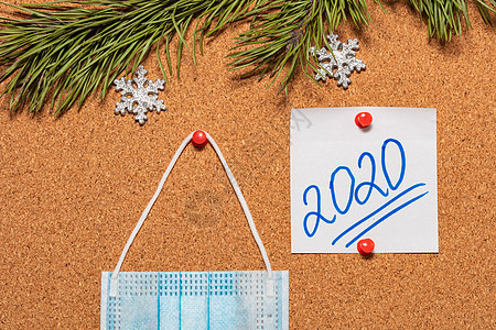 医用面具和带有 2020 年的白色便签贴在布告牌上 布告牌上装饰着松树枝和雪花 医疗保健 圣诞节 新年庆祝季节概念 新现实概念社背景图片