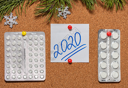 白色药丸 带有 2020 年的白色便签贴在用松树枝和雪花装饰的布告牌上 医疗保健 圣诞节 新年庆典 新常态概念 特写镜头背景图片