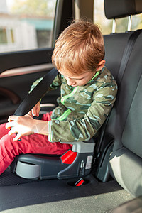小男孩坐在助推座上 试图在车上系好安全带图片