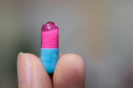 在模糊背景下展示蓝色和粉红色胶囊药片的手止痛药流感医院治疗制药科学保健女士药品药剂图片