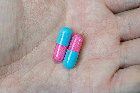 在模糊背景下展示蓝色和粉红色胶囊药片的手医院女士药店病人药理处方药物药剂治愈手指图片