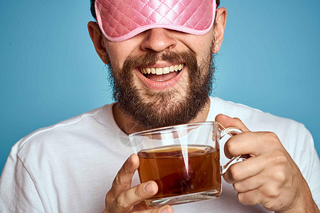 男人脸上戴着粉红睡面具 手手里拿着一杯茶 种植近视蓝底背景工作男性工作室咖啡男生胡须商业饮料头发杯子图片
