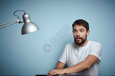一名男子 在蓝背景和灯灯办公室的桌子上用笔记本电脑互联网情感创造力职场房间成人男人商务设计师人士图片