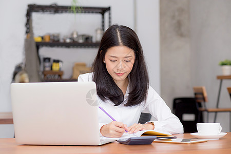 亚洲女商务人士用笔记本电脑在桌上的笔记本上写字 g职场店铺预算手机键盘女性办公室教育工作女士图片