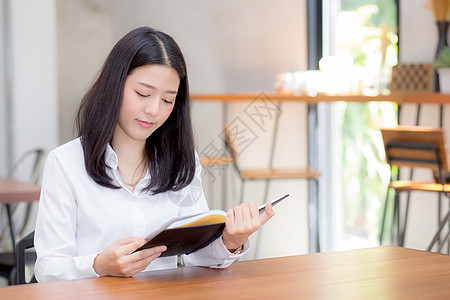 美丽的商业女青年 在小报上读笔记本工作办公室手机文书女性数据金融预算键盘咖啡店图片