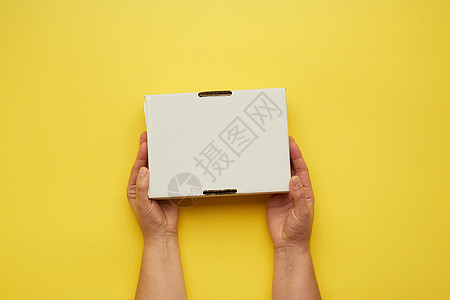 两只雌性手拿着黄色背景的 封闭纸盒图片