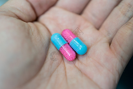 在模糊背景下展示蓝色和粉红色胶囊药片的手流感疾病疼痛医院治愈科学药品卫生处方药剂图片