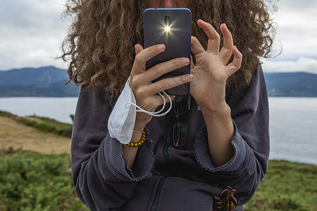 一个年轻女子 戴着面罩和智能手机 在西班牙运动衫射线女士头发互联网照片摄影卷曲衣服面具图片