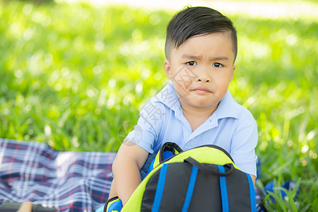 年幼的亚洲小孩笑着 在草坪上打开背包 Asia情感幸福配件地面快乐乐趣草地学校童年儿童图片