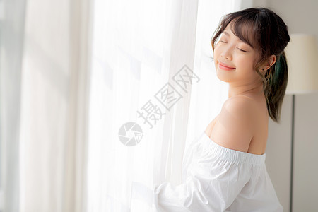 美丽的年轻亚洲女人的肖像 站在窗前女士成人酒店房间女性唤醒微笑休息女孩房子图片