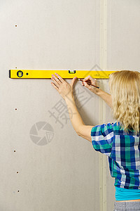 金发碧眼的年轻有吸引力的女人 利用精神水平来测量石膏墙壁上的尺寸成人头发白色工作女孩工具维修建筑层面铅笔图片