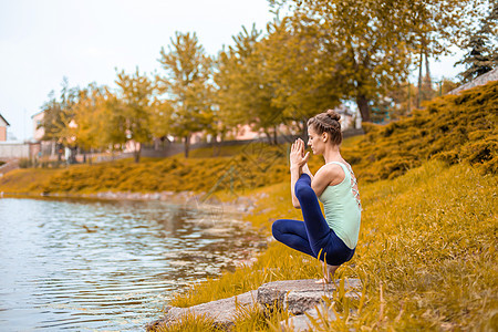 一名年轻运动女运动员在河边的黄草坪上做瑜伽 使用瑜伽类动物的姿势力量健身房瑜珈沉思体操女孩哈达海滩生活方式灵活性图片