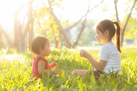 美丽的年青年轻小孩 夏天在公园玩耍的时候坐在公园里闲暇朋友们微笑女孩孩子们姐姐幸福快乐童年晴天图片