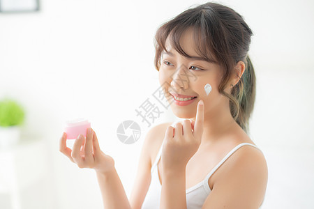 美丽的年轻的年轻女士 快乐地施用奶油或乳液皮肤护理洗剂保湿美容治疗微笑女性化妆品房间图片