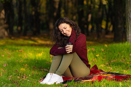 美丽的女孩享受秋天和大自然的美丽 坐在一个女士公园微笑毯子快乐格子季节树叶晴天饮料图片